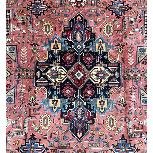 135 - A Persian Heriz woollen hand knotted carpet with stylised floral central medallion on a pink ground ... 