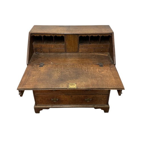 1099 - An early 19th century country house oak bureau, the fall-flap enclosing a fitted interior above four... 