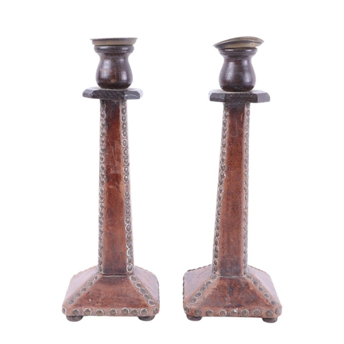 581 - A pair of Arts & Crafts oak leather covered brass studded candlesticks, 32cms high; together with tw... 