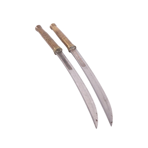 83 - An early 20th century pair of Burmese Dha knives with brass worked handles, the steel blades with si... 