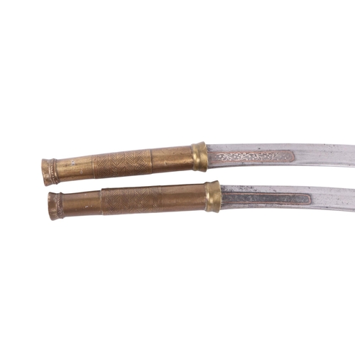 83 - An early 20th century pair of Burmese Dha knives with brass worked handles, the steel blades with si... 