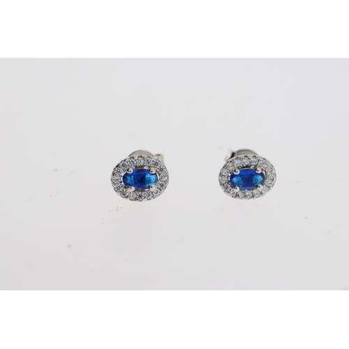 1084 - Pair of silver oval cluster studs with central blue CZ and halo of white round CZs