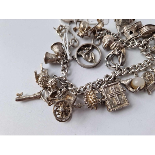 77 - A heavy silver charm bracelet with 20 silver charms 85g