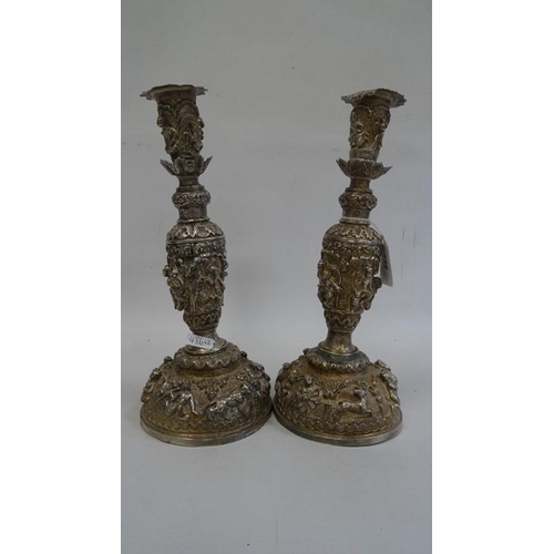 486 - A pair of Indian/Burmese white coloured metal candlesticks, relief of warriors/hunters and animals, ... 