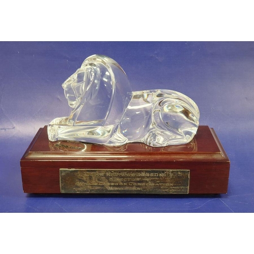 78 - A Steuben art glass model of a recumbent lion designed by Lloyd Atkins, with wooden plinth base, the... 