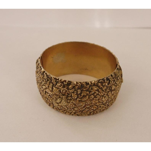 414 - Gilt-metal wide bangle, allover foliate scroll relief decorated