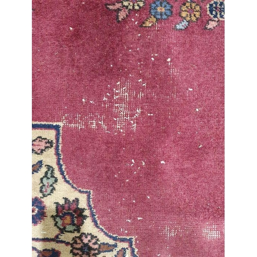 1038 - Persian-style carpet having shaped oval floral central medallion to the maroon ground, cream spandre... 