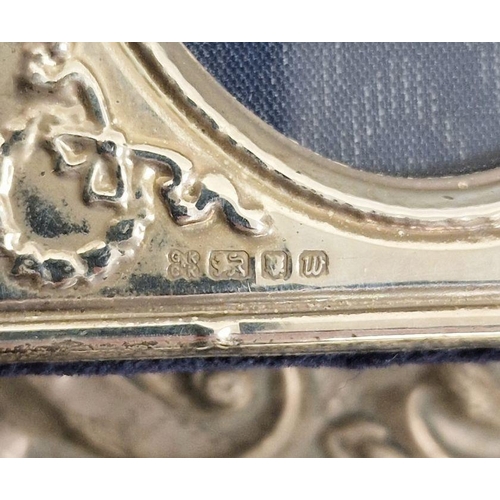 303 - Two silver backed dressing mirrors, one repousse decorated, a miniature silver mounted picture frame... 