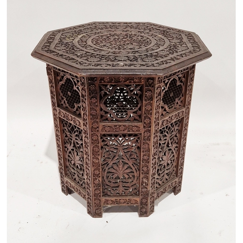 1081 - Indian hardwood octagonal folding table, the top profusely carved with scrolling foliage, on a foldi... 