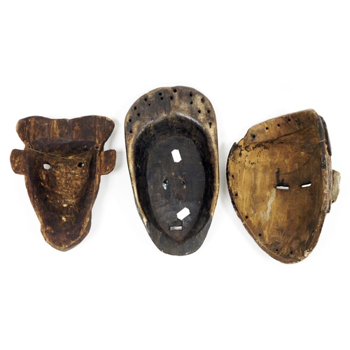 124 - Three ethnic wooden carved face masks, one with mottled blue finish and another with a white finish,... 