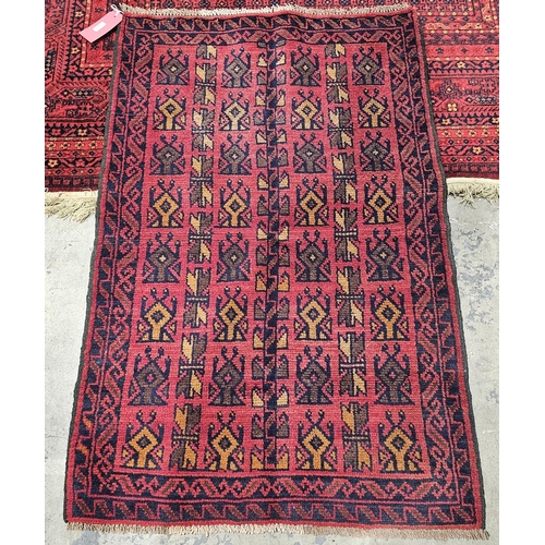 1385 - Woollen Baluchi rug with a geometric pattern on a red ground, 130cm x 85cm