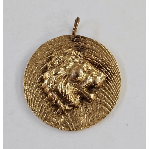 504 - Yellow metal pendant of circular form, modelled with a lion's head on a textured ground, unmarked (t... 