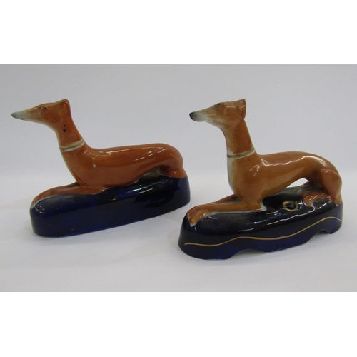 52 - Pair of Staffordshire pottery greyhound pen rests, each ochre coloured hound seated on a dark blue m... 