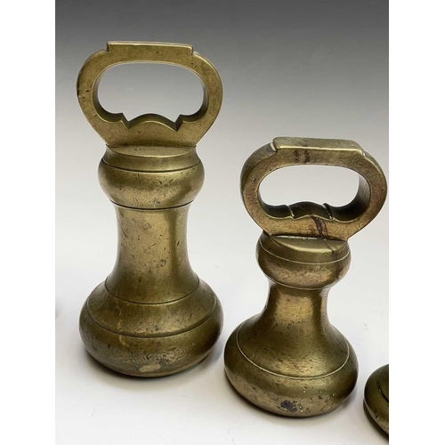 144 - A group of nine brass bell weights, 7LB to 1/2OZ, the biggest height 18.5cm, together with a nest of... 