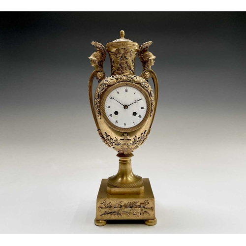 2918 - A French Empire ormolu cased mantel clock, of urn form, the covered rim applied with two winged cher... 