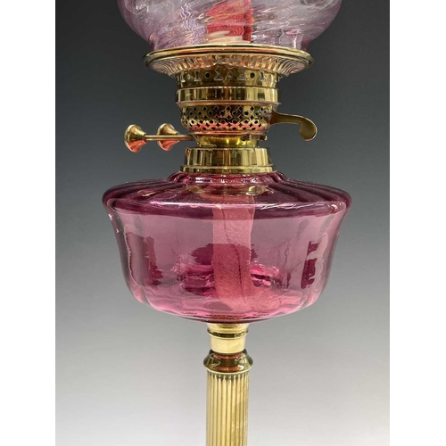 300 - A Victorian cranberry glass and brass oil lamp, with spiral fluted shade and column support, overall... 