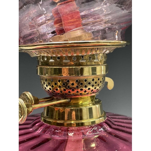 300 - A Victorian cranberry glass and brass oil lamp, with spiral fluted shade and column support, overall... 