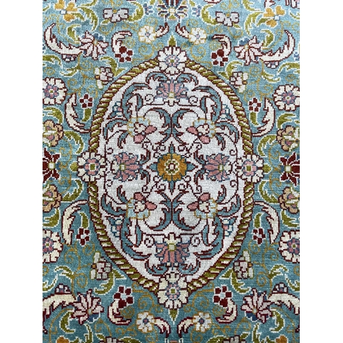 3202 - A Turkish silk rug, the pale blue field with an oval ivory medallion with scrolling flowering leafy ... 