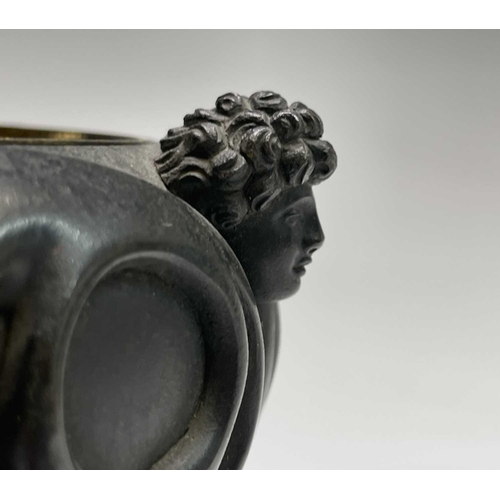 407 - A Regency bronze inkwell with cover, the lid surmounted by the figure of Cupid, the base cast with t... 