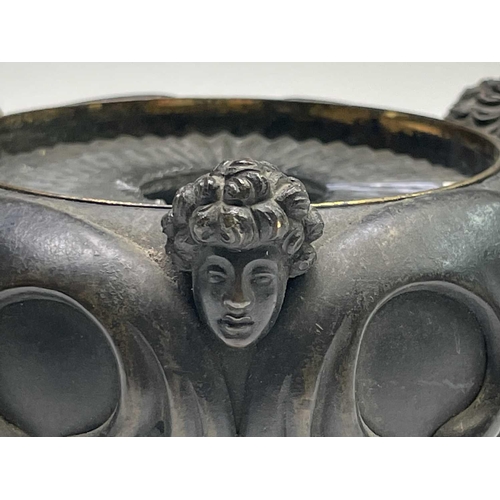 407 - A Regency bronze inkwell with cover, the lid surmounted by the figure of Cupid, the base cast with t... 