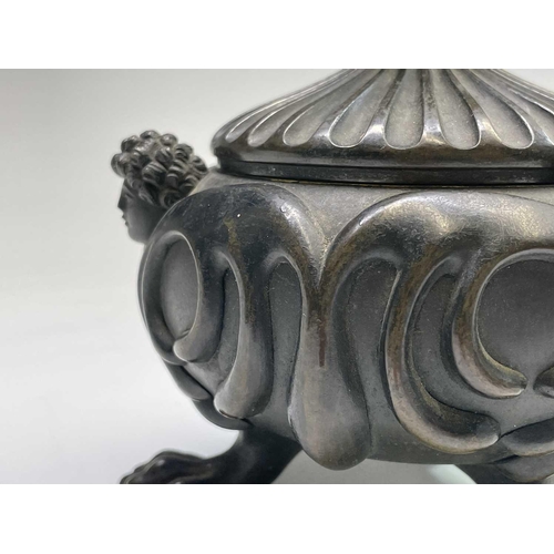 407 - A Regency bronze inkwell with cover, the lid surmounted by the figure of Cupid, the base cast with t... 