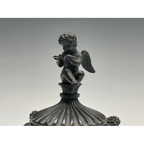 407 - A Regency bronze inkwell with cover, the lid surmounted by the figure of Cupid, the base cast with t... 