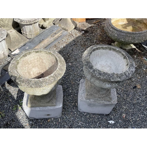 603 - A pair of composition garden urns on associated cast concrete stands. Overall height 63cm.