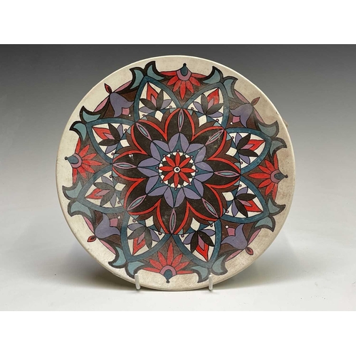 832 - A studio pottery unglazed plate, painted with a geometric floral design, the back indistinctly signe... 