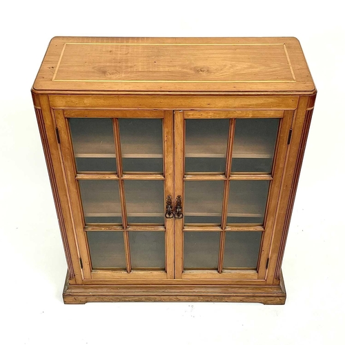 3002 - An Arts and crafts Cotswold school walnut glazed bookcase, the sycamore banded top with rounded corn... 