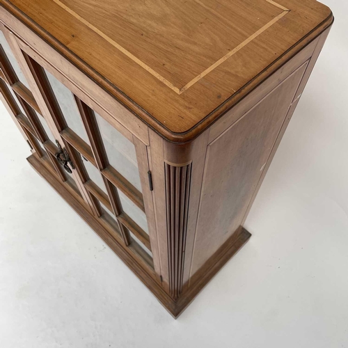 3002 - An Arts and crafts Cotswold school walnut glazed bookcase, the sycamore banded top with rounded corn... 