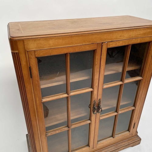 3002 - An Arts and crafts Cotswold school walnut glazed bookcase, the sycamore banded top with rounded corn... 