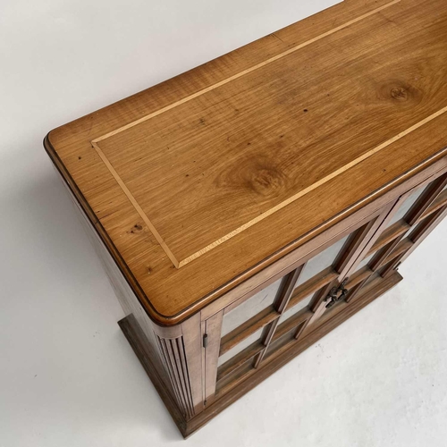 3002 - An Arts and crafts Cotswold school walnut glazed bookcase, the sycamore banded top with rounded corn... 