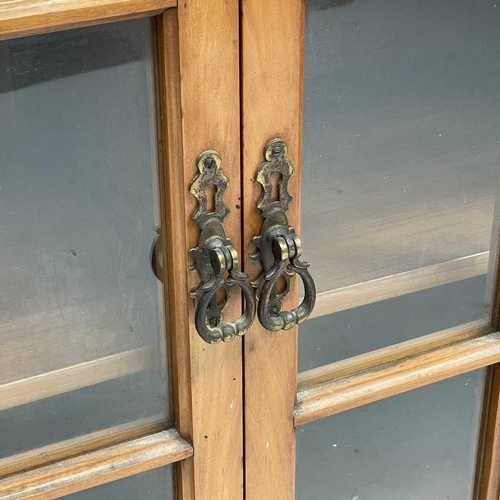 3002 - An Arts and crafts Cotswold school walnut glazed bookcase, the sycamore banded top with rounded corn... 