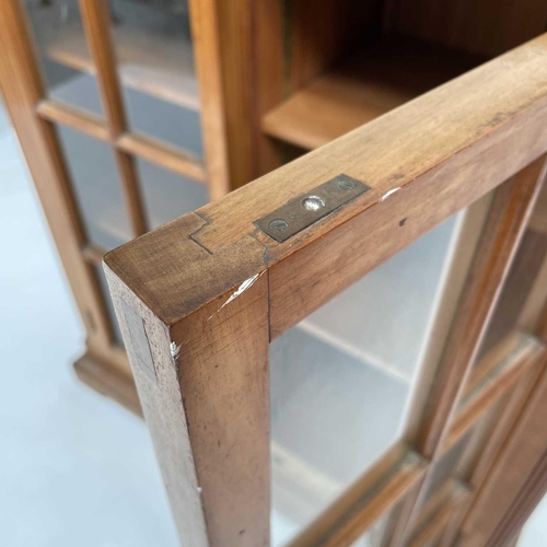 3002 - An Arts and crafts Cotswold school walnut glazed bookcase, the sycamore banded top with rounded corn... 