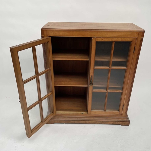 3002 - An Arts and crafts Cotswold school walnut glazed bookcase, the sycamore banded top with rounded corn... 