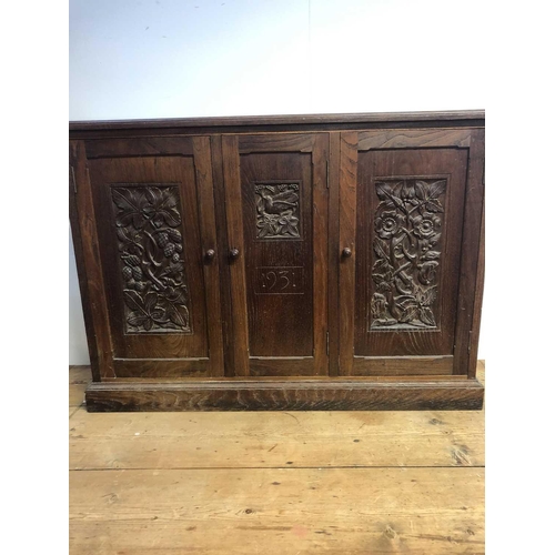 1804 - An Arts and Crafts oak cupboard, dated 1931, with three doors carved with hops, flowers and a bird, ... 