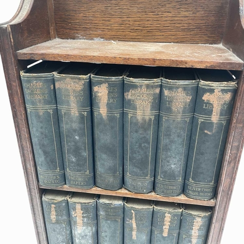 1825 - An oak narrow bookcase, early 20th century, containing 18 volumes of the Charles Dickens library, he... 