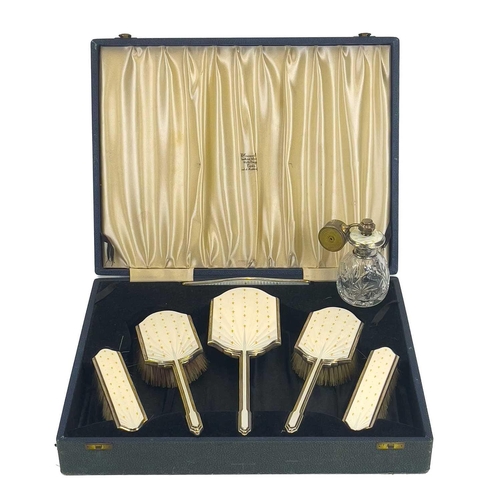 110 - A George VI silver and enamel dressing table set, cased. The five-piece set decorated with gilt fleu... 