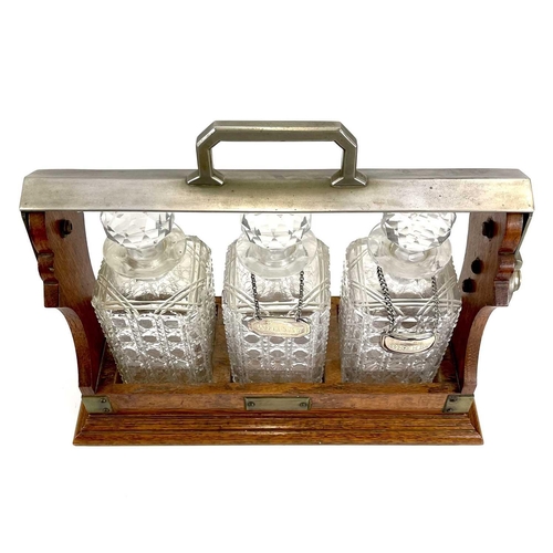 122 - An Edwardian oak three bottle tantalus. With a silver plated locking bar, height 31cm, width 38cm.