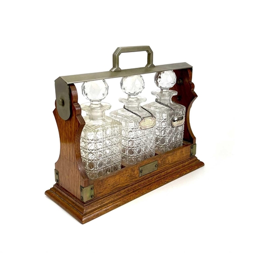 122 - An Edwardian oak three bottle tantalus. With a silver plated locking bar, height 31cm, width 38cm.