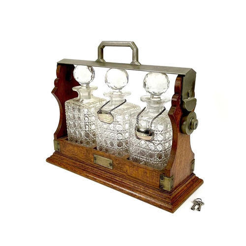 122 - An Edwardian oak three bottle tantalus. With a silver plated locking bar, height 31cm, width 38cm.