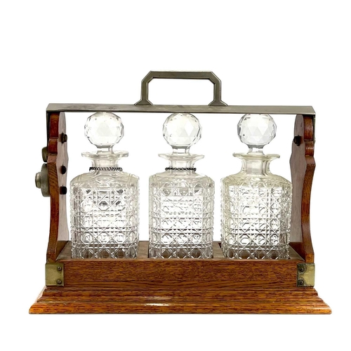 122 - An Edwardian oak three bottle tantalus. With a silver plated locking bar, height 31cm, width 38cm.