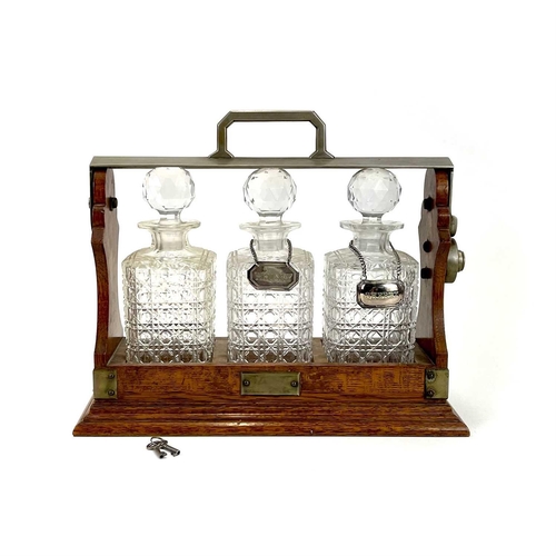 122 - An Edwardian oak three bottle tantalus. With a silver plated locking bar, height 31cm, width 38cm.