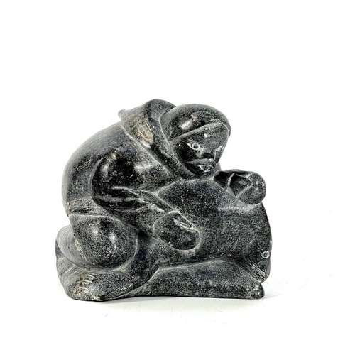 132 - A 20th century Inuit carved soapstone sculpture. Of a man holding a seal, having incised signature S... 