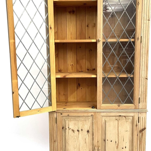 1822 - A pine display cabinet. 20th century, with two glazed doors enclosing shelves and with panel doors b... 