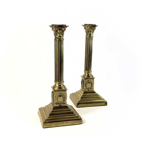 260 - A pair of brass Corinthian column candlesticks. Topped with acanthus scrolls on a stepped plinth bas... 