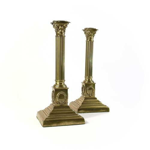 260 - A pair of brass Corinthian column candlesticks. Topped with acanthus scrolls on a stepped plinth bas... 