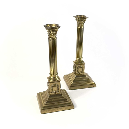 260 - A pair of brass Corinthian column candlesticks. Topped with acanthus scrolls on a stepped plinth bas... 