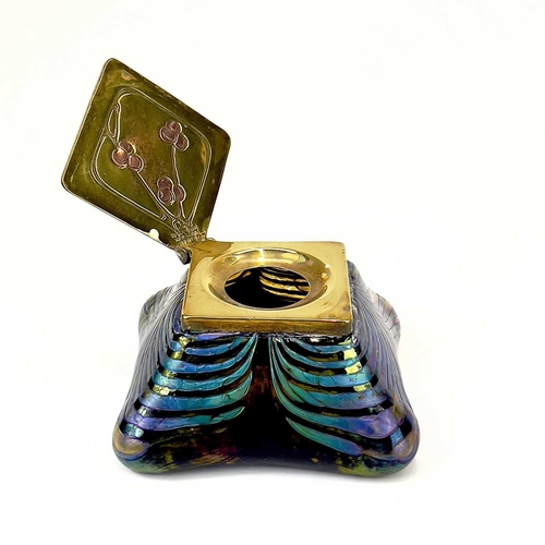 415 - An iridescent glass inkwell, probably Loetz. The lozenge shape brass cover inlaid in copper with ber... 