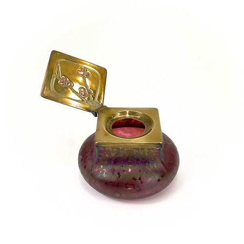 423 - A Loetz type ruby iridescent glass inkwell. The lozenge shaped brass cover inset with copper berries... 